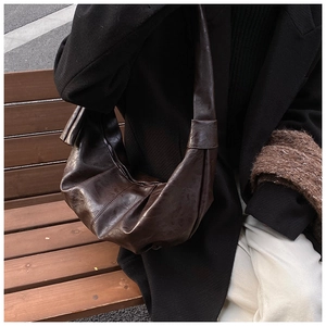 Detail of dark brown pleated croissant bag in glossy leather on a wooden bench