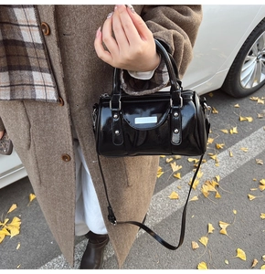 Detail of black patent leather cylinder bag with silver rivets and metallic luster