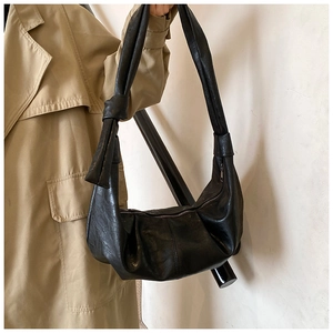 Detail of black pleated hobo bag with knotted shoulder strap worn over trench coat