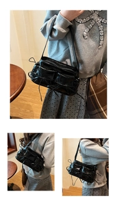 Close-up of black glossy shoulder bag with multiple utility pockets and bow detail