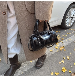 Detail of black glossy cylinder bag with silver studs and detachable strap in autumn