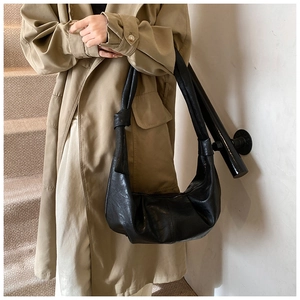 Close-up of black croissant bag with knotted strap detail paired with a trench coat
