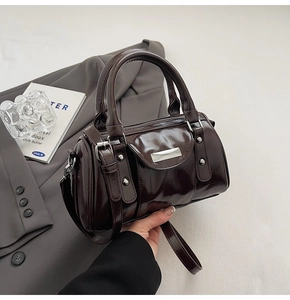 Detail of dark brown patent leather cylinder bag with polished metal logo and rivets