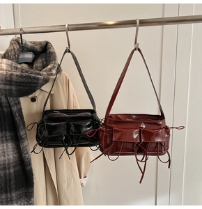 Close-up of glossy patent leather shoulder bag with decorative ribbons and utility pockets