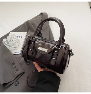 Detail of a dark brown cylindrical Boston bag with glossy finish and silver hardware