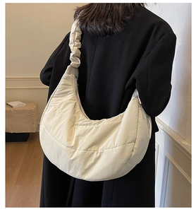 Detail of off-white quilted dumpling bag with scrunchie strap on black coat