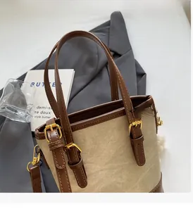 Détail du sac seau en toile montrant les anses en cuir et les boucles dorées haut de gamme