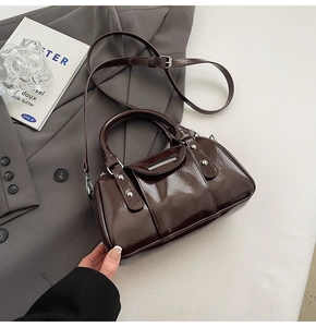 Detail of a dark brown patent leather cylinder bag with silver metal trim and adjustable strap