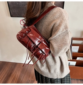 Detail of burgundy glossy leather shoulder bag with decorative tassels and wide strap