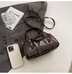 Detailed view of dark brown patent leather cylinder bag with silver metal rivets on fabric