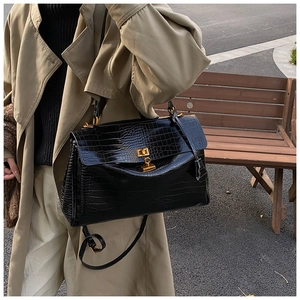 Dettaglio borsa nera con trama a coccodrillo e chiusura dorata su cappotto beige