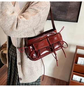 Detail view of burgundy glossy leather shoulder bag with side pockets and decorative tassels