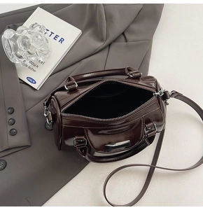 Detail of a dark brown glossy barrel bag with silver zipper on a gray blazer suit