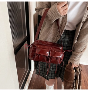 Close-up of wine red patent leather shoulder bag with vintage pocket and ribbon detail