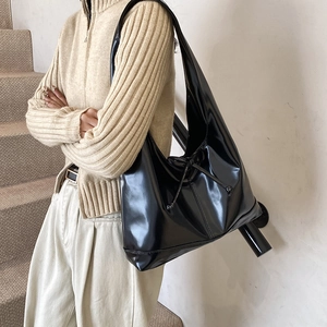 Glossy black faux leather hobo bag with bow detail worn by a model in casual style