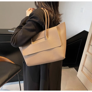 Sac fourre-tout beige chic en cuir grainé lychee porté avec un blazer noir élégant