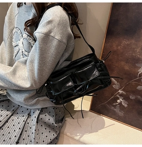 Detail of a black glossy shoulder bag with bow drawstrings styled on a model outfit