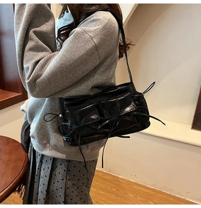 Detail of black patent leather shoulder bag with functional pockets and drawstring knots
