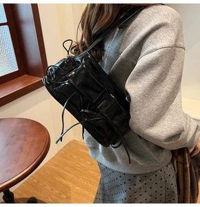 Chic black patent leather shoulder bag with decorative bow ties shown on a model