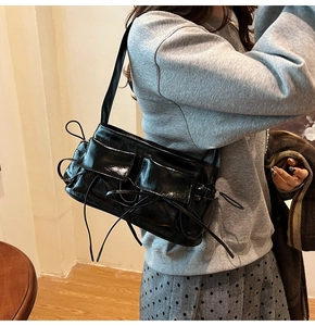 Detail of black patent leather shoulder bag with multi-pocket design and ribbon decor