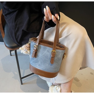 Détail du sac seau en denim bleu avec cuir marron et pendentif en peluche