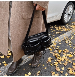 Detail of a black patent leather multi-pocket shoulder bag with glossy finish and zippers