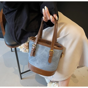 Détail du sac seau en denim bleu et cuir marron avec pompon en fourrure et logo