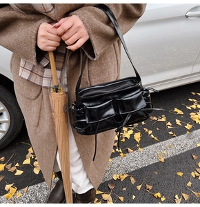 Detail of black glossy shoulder bag with multiple pockets and long ribbons in autumn setting