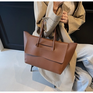 Détail d'un sac cabas marron en cuir grainé lychee porté avec un trench-coat classique
