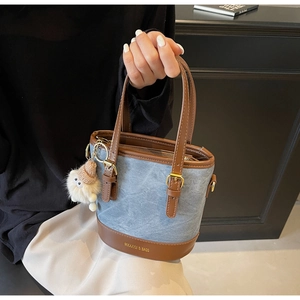 Détail du sac seau en denim avec garniture en cuir et breloque peluche décorative
