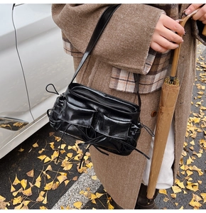 Detail of black glossy crinkled leather shoulder bag with vintage ribbon pockets