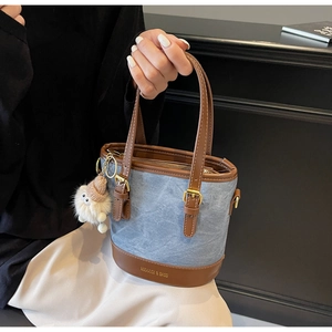 Gros plan du sac seau en denim bleu avec cuir marron et breloque ours en peluche