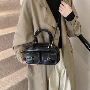 Chic black shiny bowling handbag with golden buckles shown on a model in a trench coat