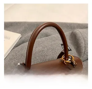 Detail of soft brown leather handbag handle with vintage coin charm and plush ball accessory