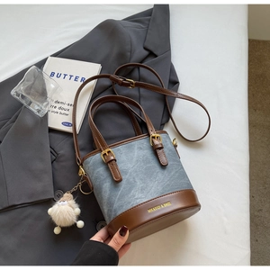 Détail d'un sac seau en tissu gris avec garniture en cuir marron et breloque peluche