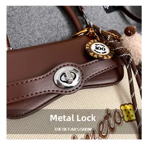 Close-up of the silver metal turn-lock on a brown leather and canvas crossbody bag