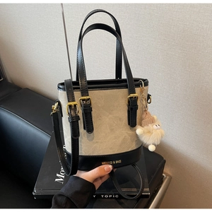 Détail du sac seau en toile avec garniture en cuir, lettrage de marque et charm peluche