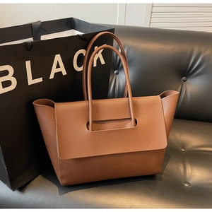Détail du sac cabas en cuir marron grainé posé sur un canapé montrant le rabat à boucle