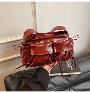 Detail of burgundy glossy pleated leather handbag with front pockets and string accents