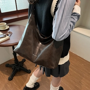 Brown leather large tote bag shown on shoulder in a stylish cafe setting