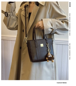 Detail of vintage brown tote bag with metal buckle and plush monster charm on khaki coat