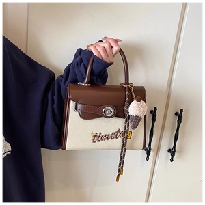 Close-up of leather canvas bag with embroidered text, twist lock and plush charm