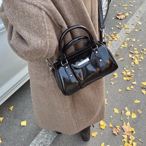Glossy black cylinder bag styled with a camel coat on a scenic autumn street