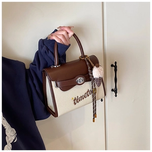 Close-up of retro canvas and brown leather handbag with embroidered text and turn-lock