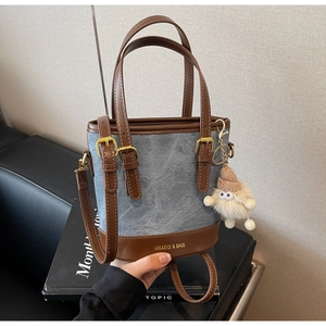 Détail du sac seau en denim bleu avec garniture en cuir marron et breloque en peluche