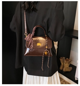 Detail of dark brown polished leather bag with silk scarf handle and golden twist lock