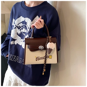 Close-up of beige canvas and brown leather flap shoulder bag with embroidery and turn-lock
