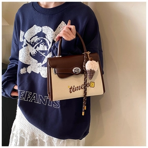 Detail of canvas shoulder bag with brown leather trim, turn-lock and plush charm