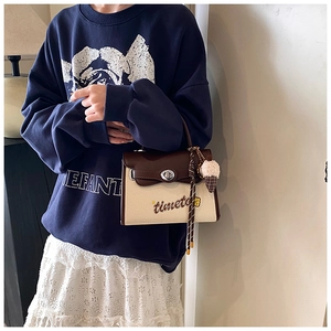 Close-up of canvas and brown leather crossbody bag with timeto embroidery and plush charm