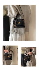 Detail of black glossy handbag featuring gold clasp, polka dot scarf, and metal charm